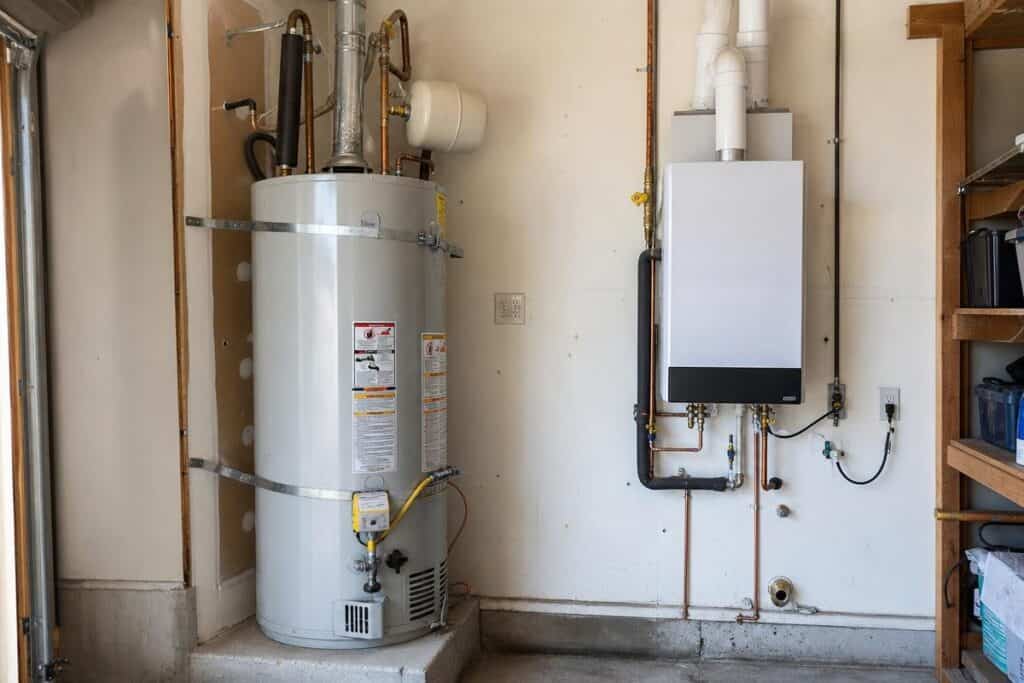A traditional tank water heater stands next to a modern tankless water heater mounted on the wall in a utility room.