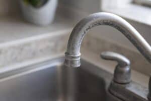 Close-up of a kitchen faucet with visible white hard water stains and mineral buildup on the metal surface.
