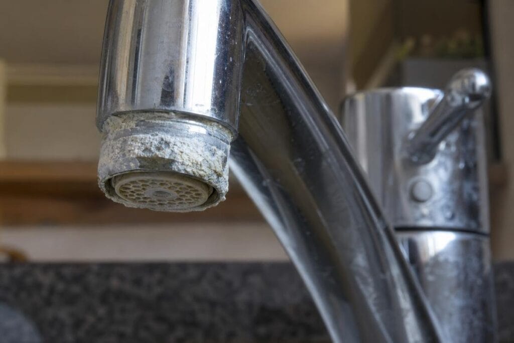 Close-up of a kitchen faucet with visible white limescale and mineral deposits around the spout.