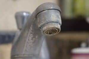 Close-up of a metal faucet with visible mineral buildup and limescale deposits around the spout, indicating hard water residue.